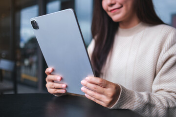 Closeup image of a woman holding and using digital tablet in cafe