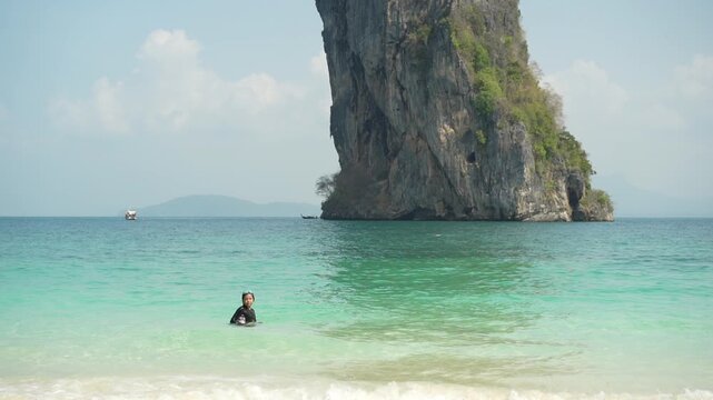 summer asian child happy playing sea water or kid girl wears swimsuit swimming goggles on blue sea with tourist boat diving at ko poda island mountain in krabi thailand for people holiday travel slow