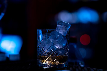 Close up glass of whiskey with ice cubes on black background with blue lights