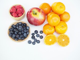 A variety of fruits including oranges, apples, blueberries, and raspberries, are placed on a whith background.