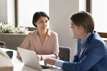 Obraz premium Confident older male manager consulting mature female client using notebook