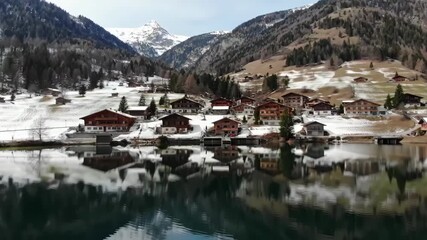 Alpine village reflects in lake, snow-covered mountains, promoting tourism and travel imagery