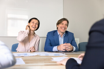 Diverse mature professionals laughing with business partners at negotiation table