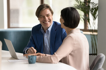 Two happy professionals collaborate on project using laptop at workplace