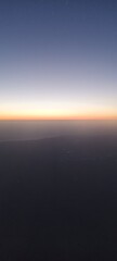 Fototapeta premium Golden Sunset Horizon Seen from Aircraft Window. Warm golden light over a fading horizon captured from an airplane, showing a calm sky transitioning from dusk to night