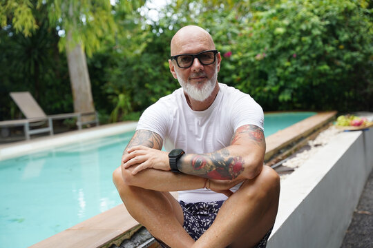 A man is comfortably sitting near a swimming pool in tropical area