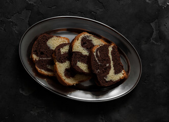 Slices of pound cake with chocolate on a metal plate on a dark background, top view