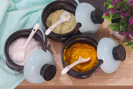 Ceramic spice jars containing fine salt, turmeric powder and seasoning powder, each with a small porcelain spoon and pastel blue lid, kitchen ingredients for cooking and food preparation
