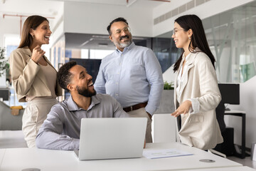 Happy diverse coworkers standing and sitting together at workplace