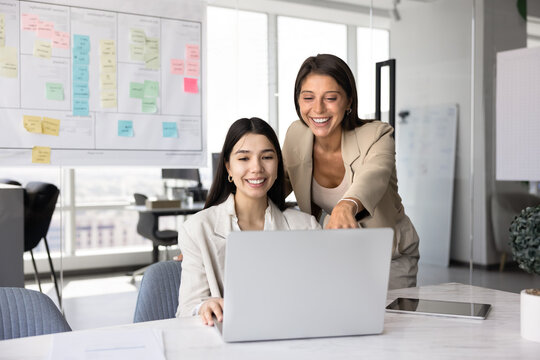 Two cheerful multiethnic office friends having fun at laptop