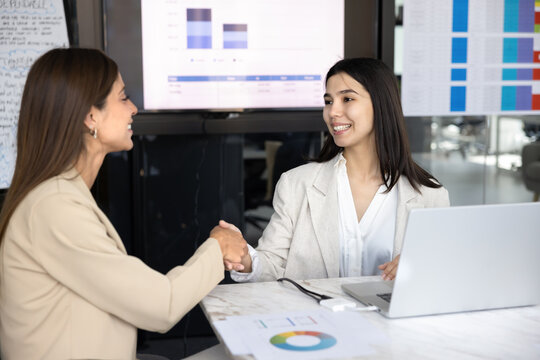 Happy young diverse female coworkers shaking hands
