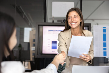 Happy young Hispanic business woman shaking hands with female coworker