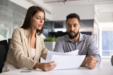 Serious young Latin business professional woman explaining paper to coworker