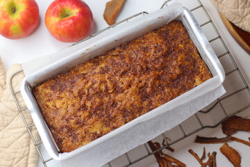 Freshly baked apple cinnamon bread loaf in a parchment lined metal pan on a cooling rack