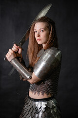 Naklejka premium Portrait of a young woman, fantasy warrior in armor with a sword in her hands isolated on a dark background