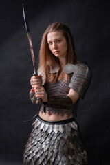 Naklejka premium Portrait of a young woman, fantasy warrior in armor with a sword in her hands isolated on a dark background