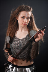 Naklejka premium Portrait of a young woman, fantasy warrior in armor with a sword in her hands isolated on a dark background