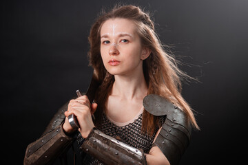 Naklejka premium Portrait of a young woman, fantasy warrior in armor with a sword in her hands isolated on a dark background