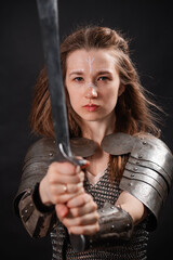 Naklejka premium Portrait of a young woman, fantasy warrior in armor with a sword in her hands isolated on a dark background