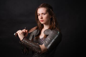 Naklejka premium Portrait of a young woman, fantasy warrior in armor with a sword in her hands isolated on a dark background