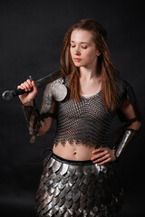 Naklejka premium Portrait of a young woman, fantasy warrior in armor with a sword in her hands isolated on a dark background