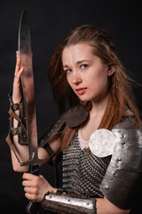 Naklejka premium Portrait of a young woman, fantasy warrior in armor with a sword in her hands isolated on a dark background