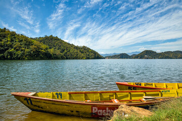 Colorful wooden boats on a peaceful lake with mountains under a bright blue sky.
