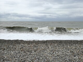 Waves crashing on a pebble beach under cloudy sky, moody seascape with gray sea and dramatic clouds, natural coastal landscape background