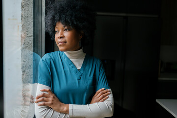 Black healthcare professional standing by window looking thoughtful