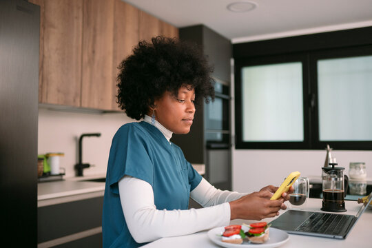 Black nurse using phone and laptop during breakfast