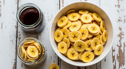 Bowl of sliced bananas with jars of banana chips and syrup on a wooden table
