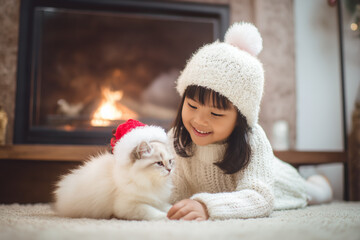Fototapeta premium Cute little asian girl hugging her cat in Christmas. Little girl in a white knitted sweater. Holiday concept. Postcard. New Year