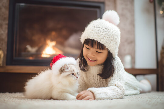 Cute little asian girl hugging her cat in Christmas. Little girl in a white knitted sweater. Holiday concept. Postcard. New Year