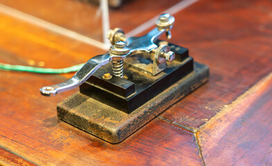 Close up of an antique or vintage chrome and black telegraph key resting on a wooden desk or surface suggesting historical communication technology