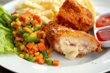 A close-up shows a plated meal of Chicken Cordon Bleu, cut to reveal melted cheese and ham. It is served with mixed vegetables, french fries, and dipping sauces.