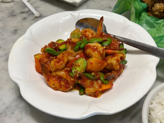 A high-angle view of Sambal Udang Petai, an Indonesian dish of prawns (udang) and stink beans (petai) stir-fried in a spicy red sambal chili sauce, served in a white bowl.