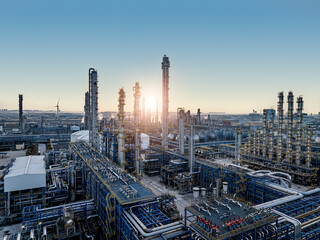 Aerial view of a large petrochemical plant with a wind turbine silhouetted against the sun at sunrise. © zhao dongfang