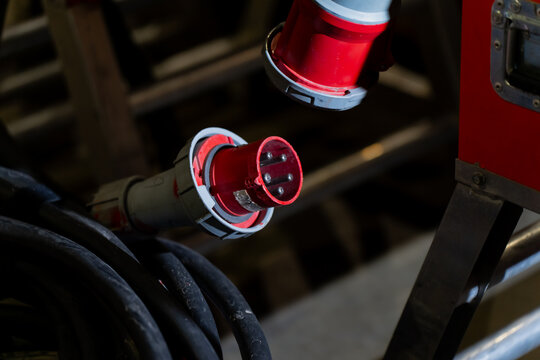 Industrial electrical connector with red casing and multi pin arrangement aligned near thick cable, highlighting robust construction and professional grade power distribution hardware