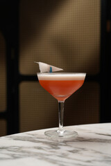 Red cocktail with foam and paper plane in a coupe glass.