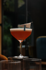 Red cocktail with foam and paper plane in a coupe glass.