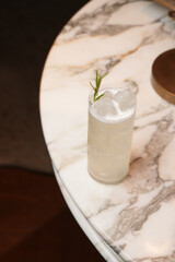 Tall, refreshing white cocktail with rosemary garnish on marble table