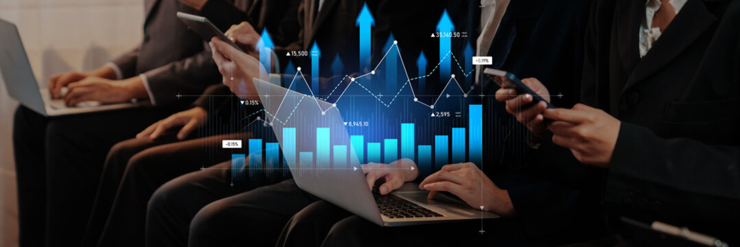 A group of business professionals using laptops and mobile devices in a modern office environment, showcasing technology and data analytics with financial graphs overlaid. Scalp