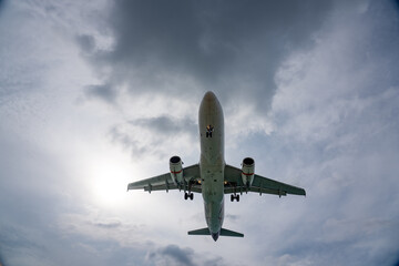 Extreme low angle view of a jet airliner descending for landing or preparing to take off set against a heavy overcast sky with a bright sunburst