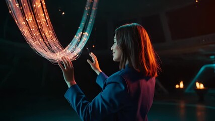 Woman touches glowing fiber optic light in dark space. Businesswoman interacts with digital light display. Woman reaches for fiber optic streams. Digital light installation with woman touching glow. - Powered by Adobe