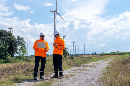 Two engineers discussing wind turbine data in a renewable energy field on a sunny day - Powered by Adobe