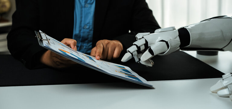 A human and a robot collaborate on data analysis in a modern office setting. The robot hand gestures toward a clipboard, emphasizing the bond of technology and business.Noogenesis - Powered by Adobe