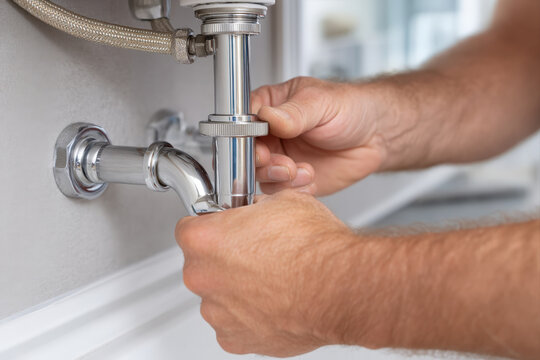 Hands installing a smart water leak sensor near washing machine valve in bright utility room