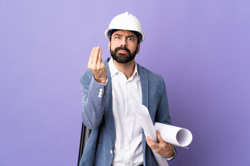 Young architect man with helmet and holding blueprints over isolated purple background making Italian gesture