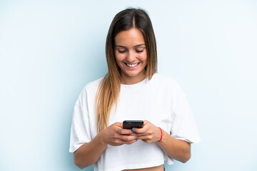 Fototapeta premium Young caucasian woman isolated on blue background sending a message or email with the mobile