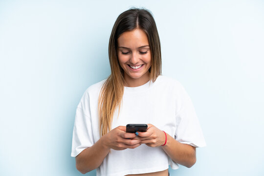 Young caucasian woman isolated on blue background sending a message or email with the mobile - Powered by Adobe